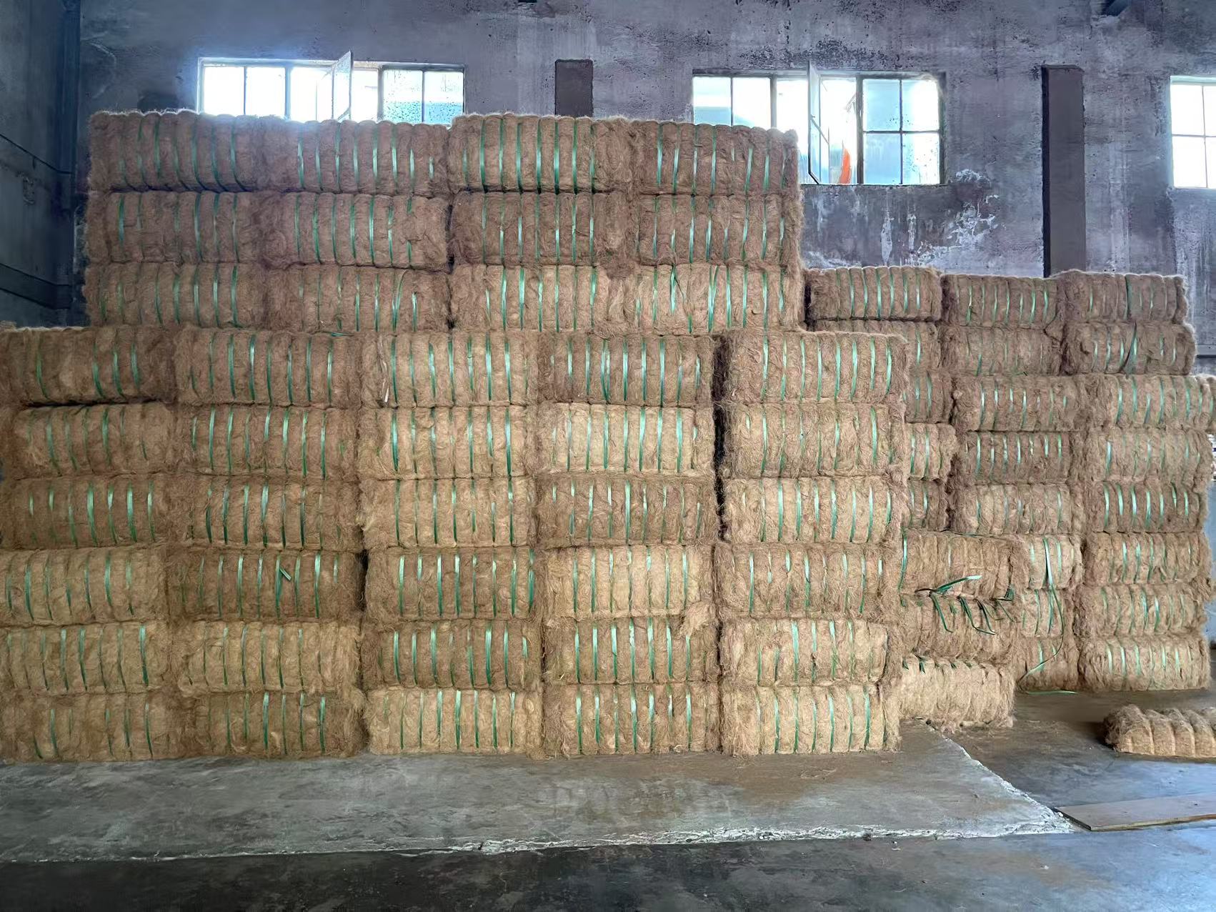 Stacks of baled wheat straw, linen, hemp, wool and bio-mass in a warehouse setting, staging for processing.